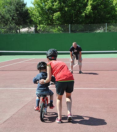 Enfant s'initiant au vélo sur un terrain de de tennis au camping en Vendée