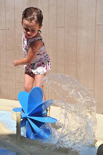 Fillette jouant avec un moulin à eau dans l'espace aquatique du camping à Saint-Hilaire-de-Riez